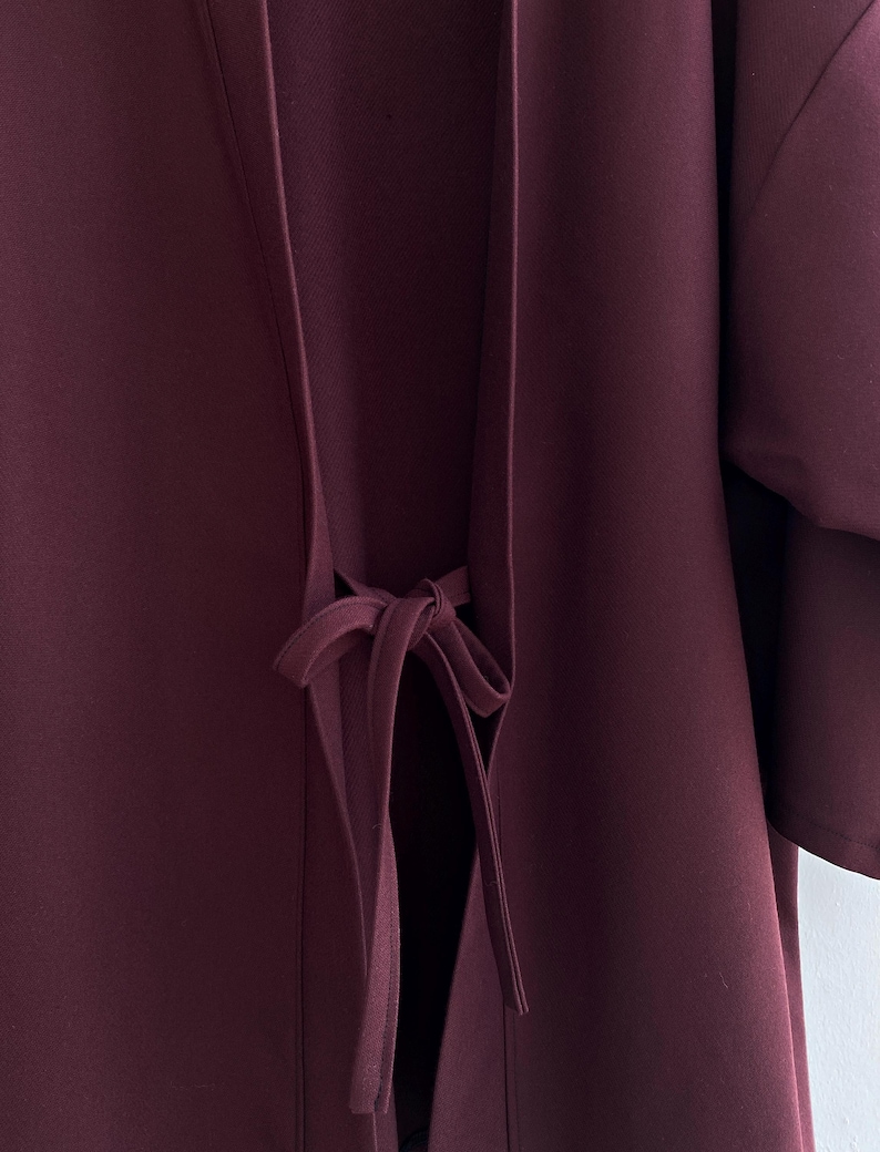 May include: A burgundy kimono with a long tie at the waist. The tie is tied in a bow at the front of the garment.