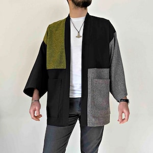 May include: A patchwork kimono-style jacket in black, olive green, and gray. The jacket has a relaxed fit with wide sleeves and two front pockets. The color-blocked design creates a modern, unique look.