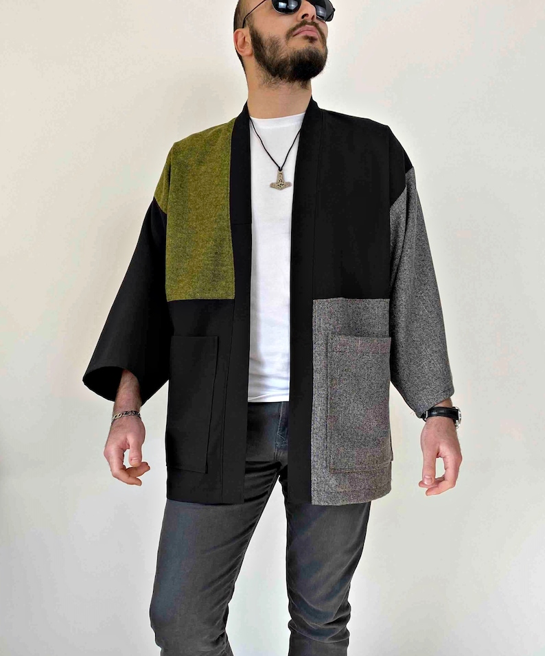 May include: A patchwork kimono-style jacket in black, olive green, and gray. The jacket has a relaxed fit with wide sleeves and two front pockets. The color-blocked design creates a modern, unique look.