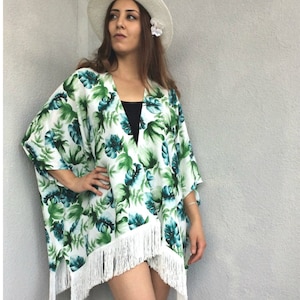 Può includere: Kimono bianco con stampa floreale verde e blu e bordino a frangia bianco.