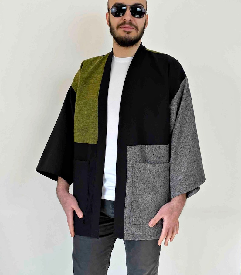 May include: A patchwork kimono-style jacket in black, olive green, and gray. The jacket features large pockets and a relaxed fit. The sleeves are wide and the garment is open in the front.