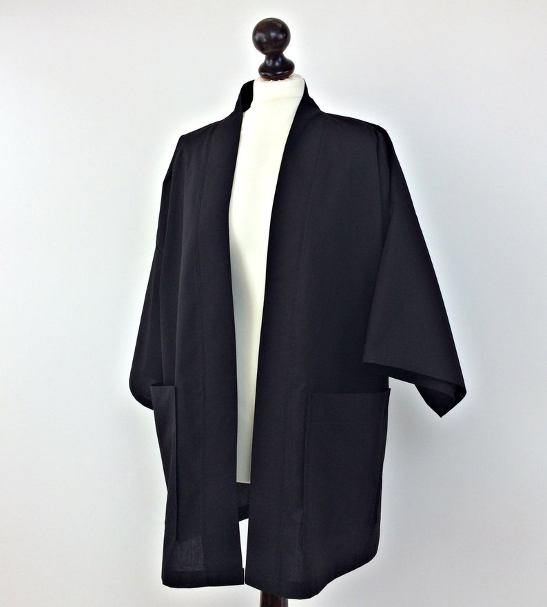 May include: A black kimono with long sleeves and two pockets. The kimono is open in the front and has a simple design.