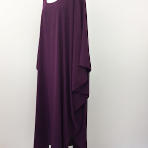 May include: A long, loose-fitting, purple maxi dress with a round neckline and long sleeves. The dress has a flowing, draped design.