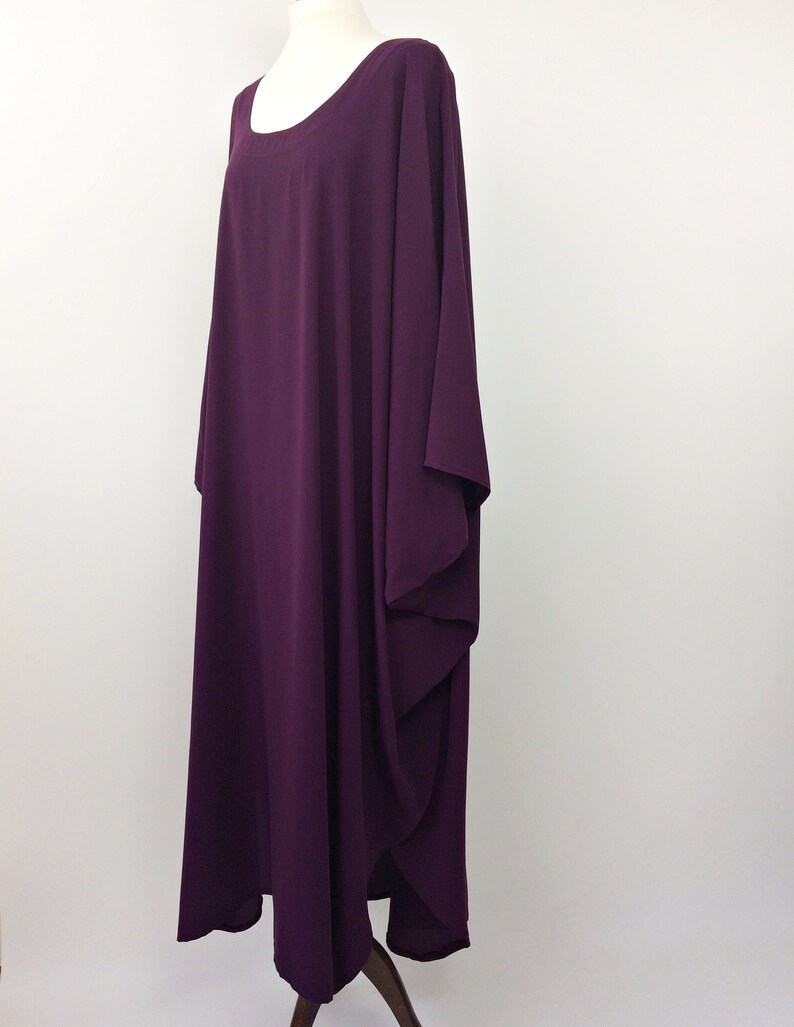 May include: A long, loose-fitting, purple maxi dress with a round neckline and long sleeves. The dress has a flowing, draped design.