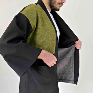 May include: A black kimono-style jacket with a green textured panel on the upper chest and shoulders. The jacket has wide sleeves and a relaxed fit. The interior lining is a gray fabric.
