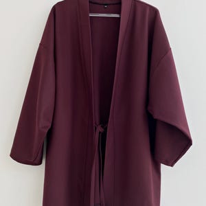 May include: A burgundy kimono-style jacket with a tie closure. The jacket has long sleeves and a relaxed fit.