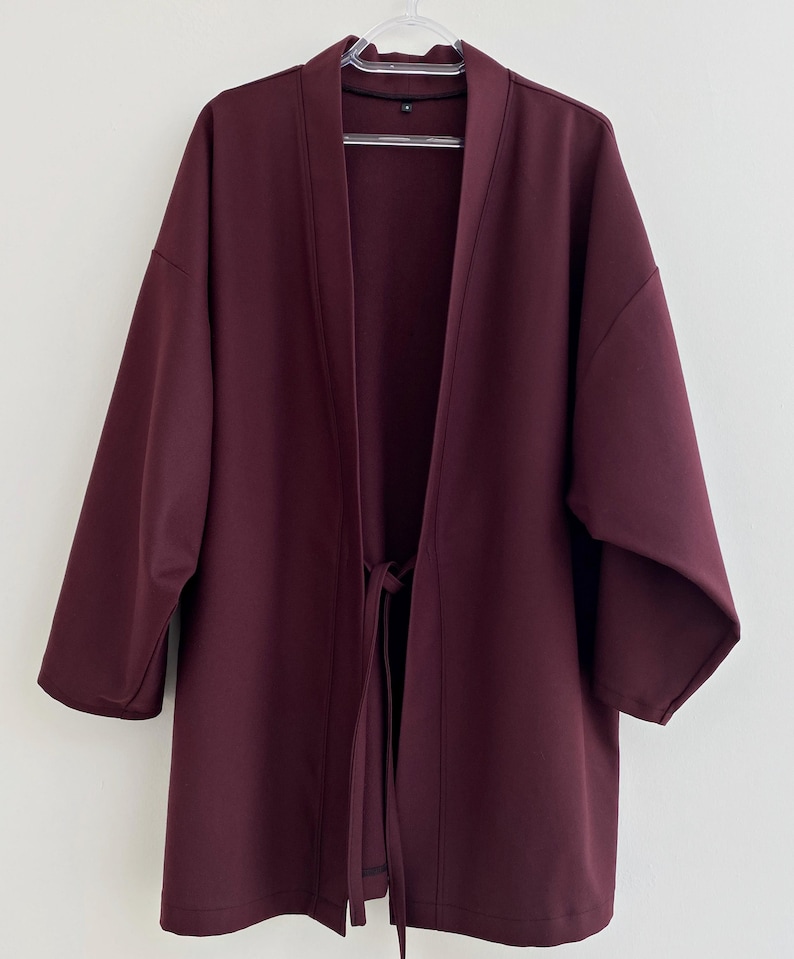 May include: A burgundy kimono-style jacket with a tie closure. The jacket has long sleeves and a relaxed fit.