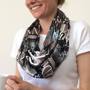 Könnte beinhalten: Ein brauner, schwarzer und blauer Infinity-Schal mit einem Druck aus verschiedenen Wörtern und Buchstaben.