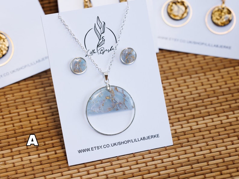 Puede incluir: Un collar de plata con un gran colgante redondo con un dise&ntilde;o marmoleado azul y dorado. El colgante est&aacute; engastado en una resina transparente. El collar viene con un par de pendientes a juego.