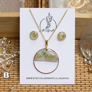 Puede incluir: Un conjunto de collar y pendientes de oro con un colgante redondo que presenta un dise&ntilde;o de resina verde y blanca con motas doradas. El colgante est&aacute; en una cadena de oro. Los pendientes son peque&ntilde;os y redondos con un dise&ntilde;o similar. El conjunto se muestra en una tarjeta blanca con el texto "Lilla Bj&ouml;rke" y "WWW.ETSY.CO.UK/SHOP/LILLABJ&Ouml;RKE".