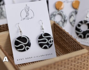 May include: A pair of black and white geometric pattern earrings with silver hooks. The earrings are displayed on a white card with the text "Lilla Bjerke" and "Etsy Shop: Lilla Bjerke".