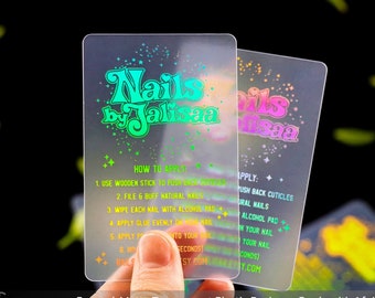 Könnte beinhalten: Zwei mattierte, transparente Plastik-Visitenkarten mit holografischen Folienakzenten. Der Text auf den Karten lautet "Nails by Jalisaa" und enthält Anweisungen zum Anbringen der Nägel.