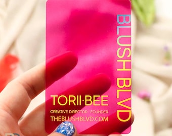 Può includere: Un biglietto da visita in plastica rosa con lettere in lamina dorata. Il testo recita "BLUSH BLVD", "TORII-BEE", "CREATIVE DIRECTOR FOUNDER" e "THEBLUSHBLVD.COM".