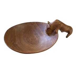 May include: A wooden serving bowl with a carved lion head handle. The bowl is oval-shaped and has a rich, brown color. The lion head is detailed and adds a unique touch to the piece.