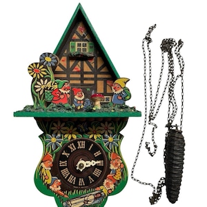 May include: A wooden cuckoo clock featuring a green frame, a house facade with three gnomes, and a clock face with Roman numerals. The clock is decorated with painted flowers and additional gnomes, and includes a hanging chain with a pinecone weight.