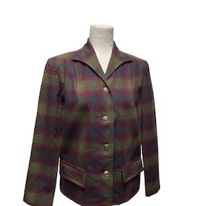 Puede incluir: Una blazer a cuadros en tonos verdes, burdeos y azul marino, exhibida en un maniquí. La chaqueta presenta un cuello con solapas, tres botones dorados y dos bolsillos delanteros. La tela tiene una apariencia texturizada.