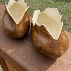 Puede incluir: Dos jarrones de cerámica marrón con forma de tulipán. Tienen un interior beige claro y un exterior marrón oscuro con textura. Los jarrones están sobre una superficie de madera.