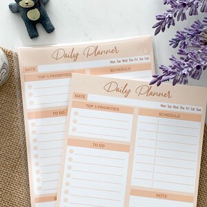 May include: Two peach-colored daily planner sheets with a white background. The top sheet has the text "Daily Planner" and the bottom sheet has the text "Daily Planner". Both sheets have sections for "Date", "Top 3 Priorities", "To Do", "Mon Tue Wed Thu Fri Sat Sun", "Schedule", and "Note".