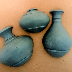 May include: Three dark green, matte-finished decorative vases with textured surfaces. Each vase features a distinct shape, including one tall, slender neck design and two shorter, rounded bulbous forms, all displaying horizontal ring details.