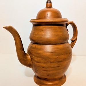 May include: A brown ceramic teapot with a lid and handle. The teapot has a curved spout and a rounded body. The surface has a wood-grain texture. The teapot is designed for serving tea.