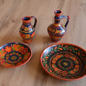 Può includere: Due brocche in ceramica dipinte a mano, blu e arancio, con un motivo floreale e due ciotole in ceramica dipinte a mano abbinate, blu e arancio, con un motivo floreale.
