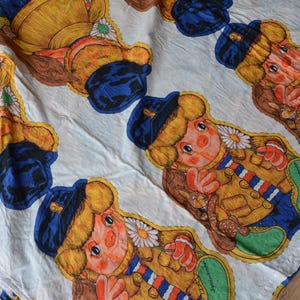 Könnte beinhalten: Weißer Stoff mit einem sich wiederholenden Muster von Cartoonfiguren. Jede Figur trägt einen gelben Mantel, eine blaue Mütze und grüne Schuhe. Die Figuren haben orangefarbene Haut, rote Handschuhe und eine Gänseblümchen auf der Brust.