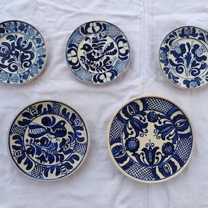 May include: Five ceramic plates with blue and white floral and bird designs. The plates vary in size and feature intricate patterns. The designs include stylized flowers, leaves, and birds, all set against a white background.