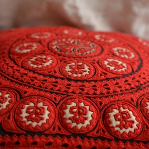 May include: Red and white embroidered throw pillow with a circular pattern. The pillow is made of a soft, textured fabric and has a delicate, intricate design.