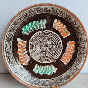 May include: A brown ceramic plate with white and black swirl designs and orange and green floral accents.