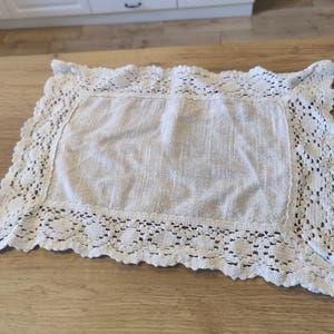 Peut inclure: Une nappe en dentelle blanche crochetée avec un motif floral délicat. La nappe est faite d'un tissu doux et léger et a un bord festonné.
