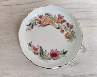 Peut inclure: Une soucoupe en céramique blanche avec un bord doré et un motif floral dans les tons rose, vert et orange.