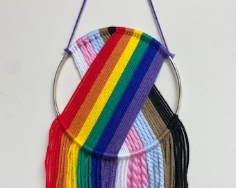 May include: A rainbow-colored yarn wall hanging with a silver ring and fringe. The colors of the yarn are red, orange, yellow, green, blue, purple, white, pink, light blue, brown, and black.
