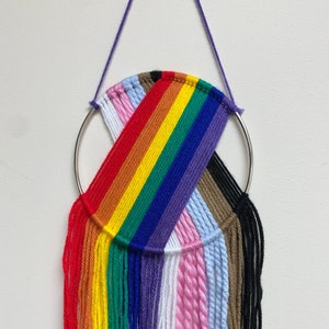 May include: A rainbow-colored yarn wall hanging with a silver ring and fringe. The colors of the yarn are red, orange, yellow, green, blue, purple, white, pink, light blue, brown, and black.