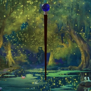 Puede incluir: Un bast&oacute;n de color marr&oacute;n oscuro con un orbe azul en la parte superior, sobre un fondo de una escena de pantano con exuberantes &aacute;rboles verdes y luces brillantes. El bast&oacute;n est&aacute; en el agua.
