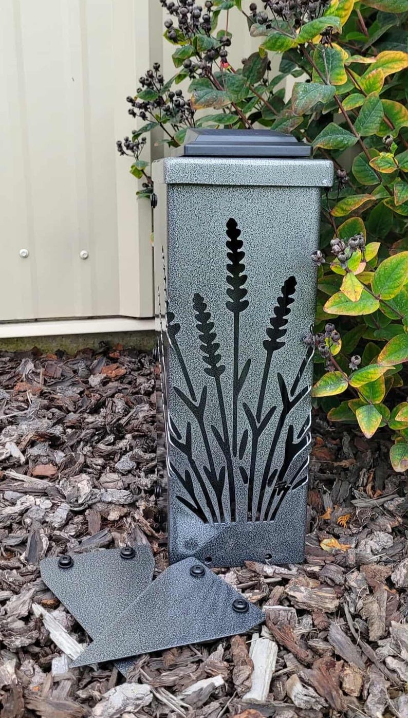 May include: A rectangular, silver-toned metal outdoor light fixture with a textured, speckled finish. The front panel features a laser-cut design of lavender stalks. Two additional matching metal plates with black fasteners are positioned in front.