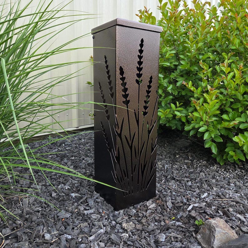 May include: A tall, rectangular, dark bronze metal garden light fixture featuring laser-cut silhouettes of lavender stalks on its front panel. The structure has a flat top and a textured finish, designed to cast light through the cutouts.
