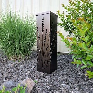 May include: A tall, rectangular, dark bronze metal outdoor light fixture featuring a laser-cut design of lavender stalks on its front panel. The structure has a flat top and a solid, clean-lined frame, designed to cast light through the cutouts.