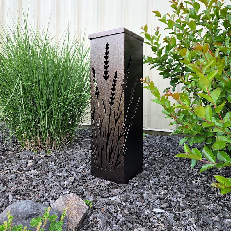 May include: A tall, rectangular, dark bronze metal outdoor light fixture featuring a laser-cut design of lavender stalks on its front panel. The structure has a flat top and a solid, clean-lined frame, designed to cast light through the cutouts.