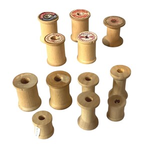 Pode incluir: Uma coleção de bobinas de madeira vintage, algumas com rótulos coloridos. As bobinas variam em tamanho e forma, com um acabamento em madeira natural. Alguns rótulos apresentam texto e elementos decorativos, adicionando um toque de nostalgia à coleção.