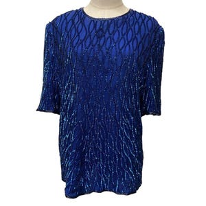 May include: A short-sleeved top in a vibrant royal blue color, fully embellished with intricate dark blue beadwork arranged in a repeating vertical wave pattern that covers the entire front and the sleeves of the garment.