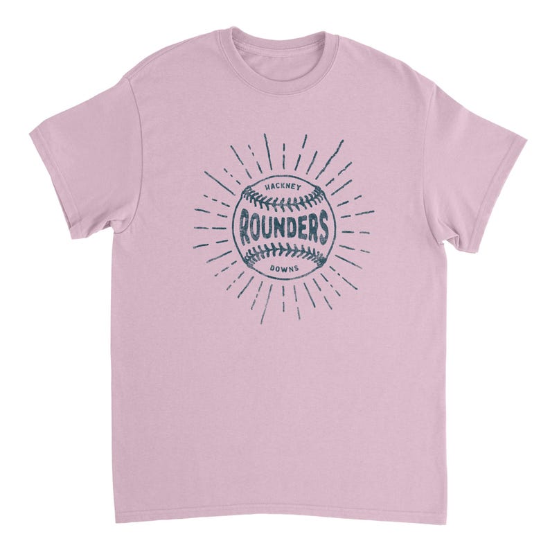 May include: A light pink short-sleeve t-shirt featuring a dark blue graphic on the chest. The graphic depicts a baseball with the text "HACKNEY" above, "ROUNDERS" in the center, and "DOWNS" below, all surrounded by radiating sunburst lines.