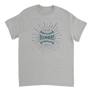 May include: A heather gray short-sleeve t-shirt featuring a dark blue graphic of a baseball with the text "HACKNEY ROUNDERS" printed in the center, surrounded by radiating lines that create a sunburst effect on the front of the garment.