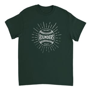May include: A dark green short-sleeve t-shirt featuring a white graphic of a baseball with the text "HACKNEY ROUNDERS DOWNS" printed across the center. The design includes radiating lines around the ball, creating a sunburst effect on the chest.