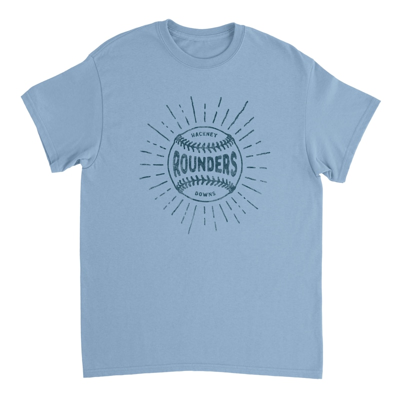 May include: A light blue short-sleeve t-shirt featuring a dark blue graphic of a baseball with the text "HACKNEY ROUNDERS DOWNS" printed across the center. The design includes radiating lines extending outward from the baseball in a sunburst pattern.