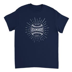 May include: A navy blue short-sleeve t-shirt featuring a white graphic of a baseball with the text "HACKNEY ROUNDERS DOWNS" printed in the center. The design includes radiating lines extending outward from the ball, creating a sunburst effect.