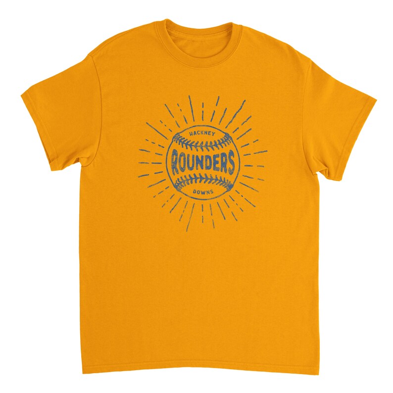 May include: A mustard yellow short-sleeve t-shirt featuring a dark blue graphic on the chest. The graphic depicts a baseball with the text "HACKNEY ROUNDERS DOWNS" printed across the center, surrounded by radiating lines in a sunburst pattern.
