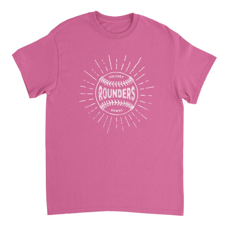 May include: A pink short-sleeved t-shirt featuring a white graphic of a baseball with the text "HACKNEY ROUNDERS" printed in the center. The design includes radiating lines extending outward from the ball, creating a sunburst effect on the chest.