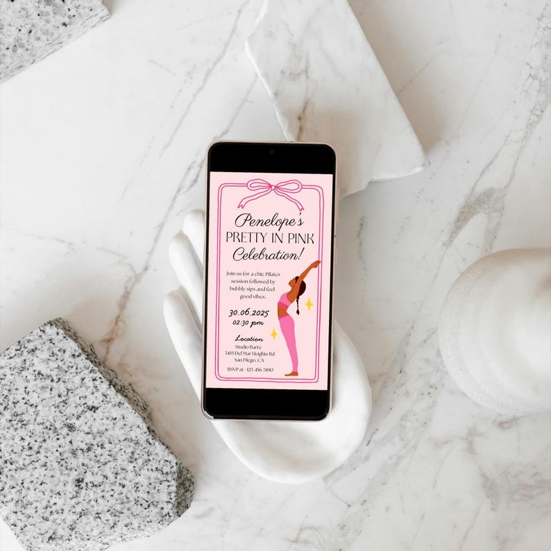 Puede incluir: Un smartphone muestra una invitaci&oacute;n rosa para "Penelope's Pretty in Pink Celebration!". La invitaci&oacute;n presenta un lazo, un gr&aacute;fico de bailarina y detalles del evento. El tel&eacute;fono se sostiene en una escultura blanca con forma de mano sobre un fondo de m&aacute;rmol.