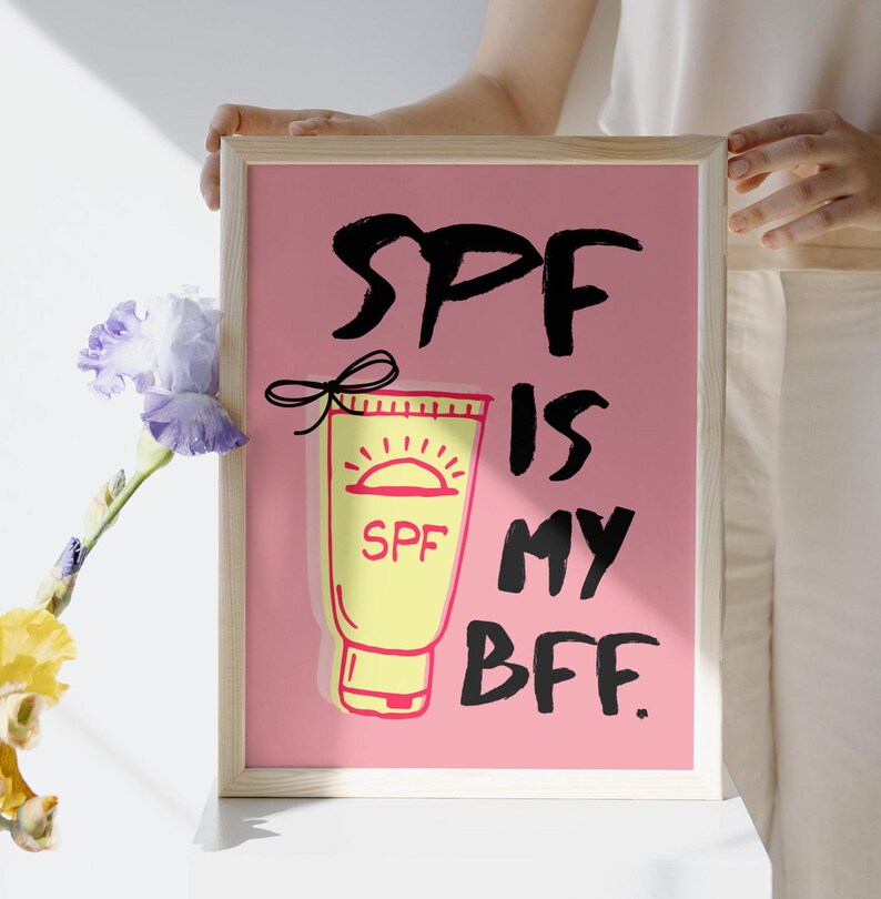 May include: A pink framed print with the text "SPF is my BFF." in black. A yellow tube of sunscreen with a red sun and the word "SPF" is pictured next to the text.