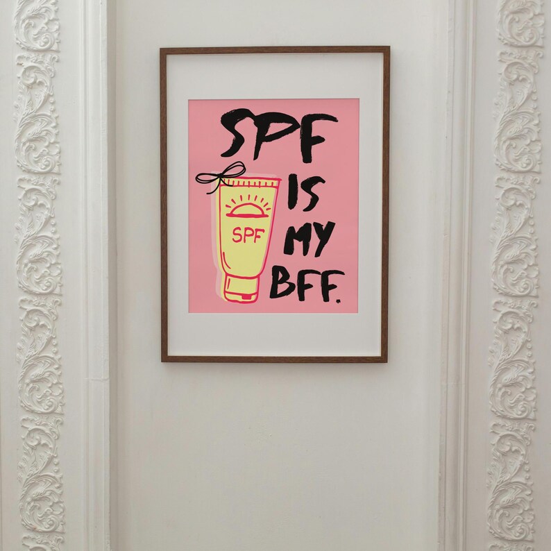 May include: A pink framed print with a white background and black text that reads "SPF is my BFF." A cartoon image of a yellow sunscreen bottle with a red sun and the word "SPF" is on the left side of the text.